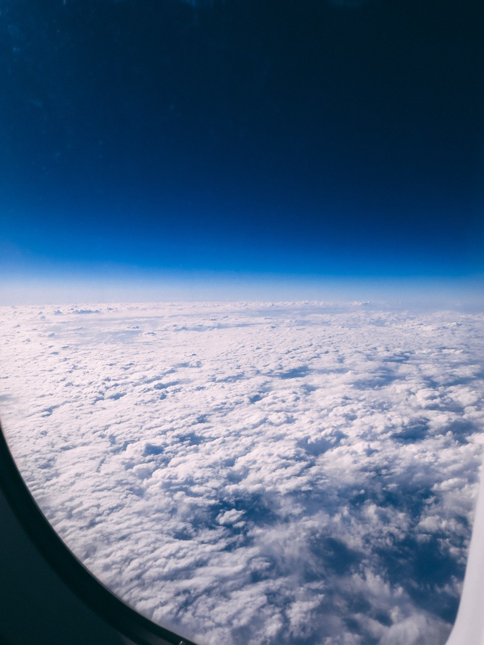 Blue sky above a sea of clouds, seen through an airplane window